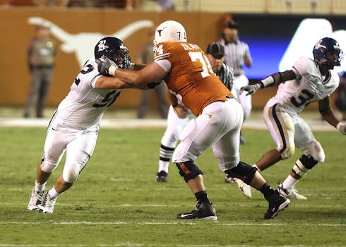 Athletes in action during an American football game on a grassy field.
