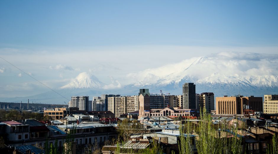 City skyline with snow-capped mountains under a blue sky, highlighting urban and natural beauty.