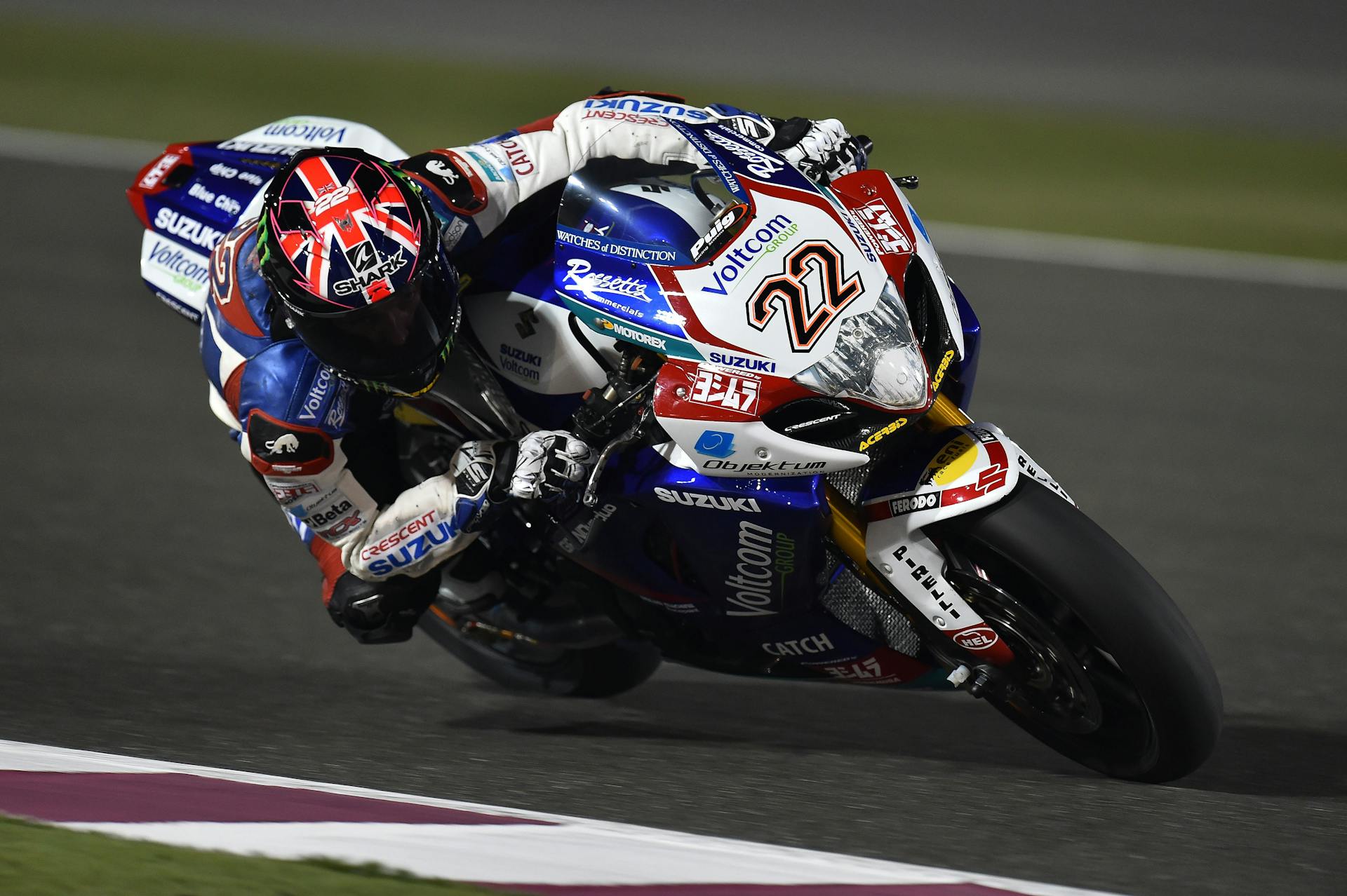 High-speed motorcycle racing action captured under night lights on an international circuit.