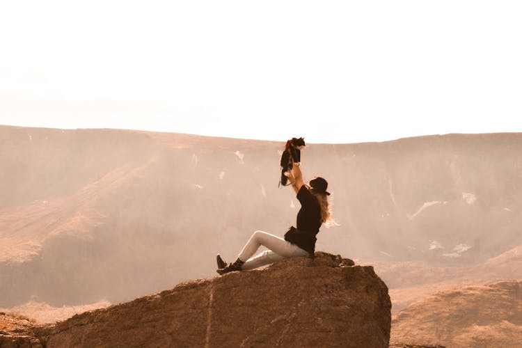 Woman Sitting On Rock And Rising Cat Over Hat