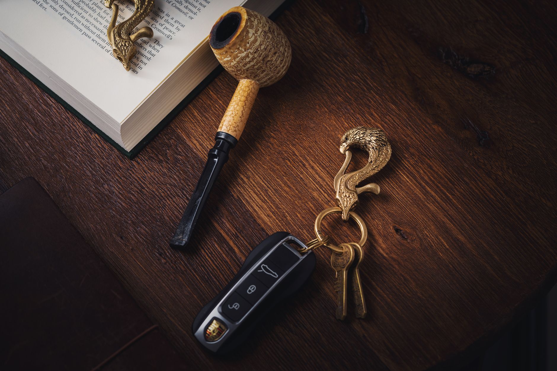 Elegant artistic arrangement of a keychain and pipe on a wooden surface with a book and keys.