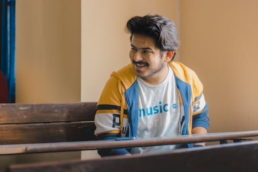 A smiling young man sitting in a classroom wearing casual attire, bright and relaxed.