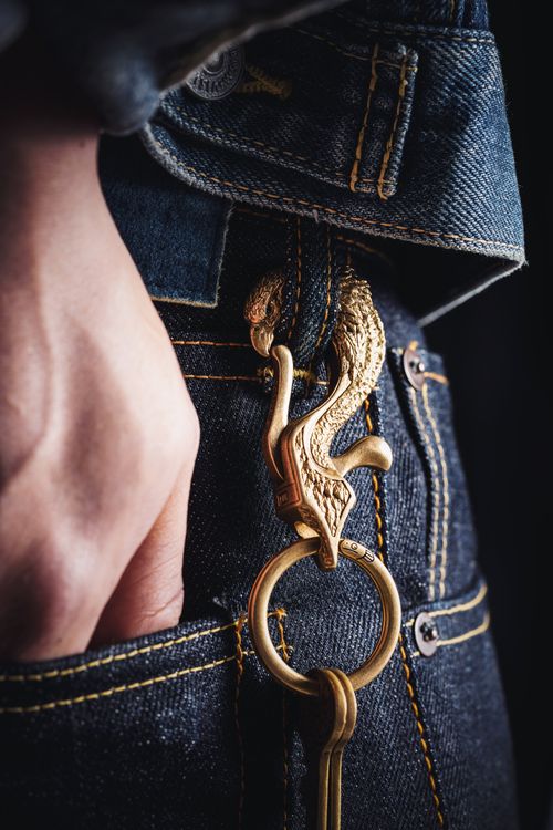Free Golden dragon keychain hanging from blue jeans pocket, artistic close-up. Stock Photo