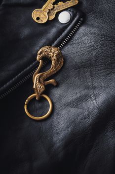 Close-up of an eagle-shaped brass keychain on a textured black leather jacket with visible keys.