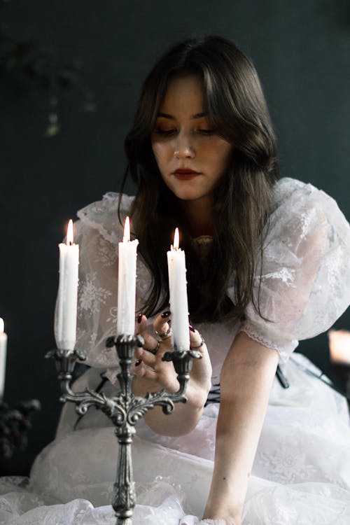 Young Brunette in a White Dress Sitting next to Candlesticks in a Vintage Candle Holder 