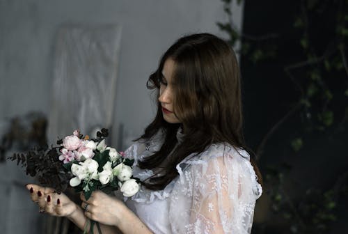 Young Brunette Wearing a White Dress Holding a Bunch of Flowers