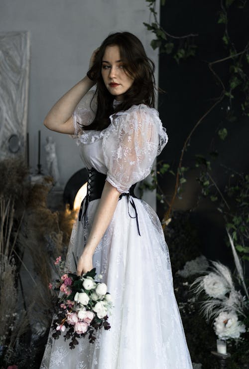 Young Brunette Wearing a White Dress with a Black Corset and Holding a Bunch of Flowers