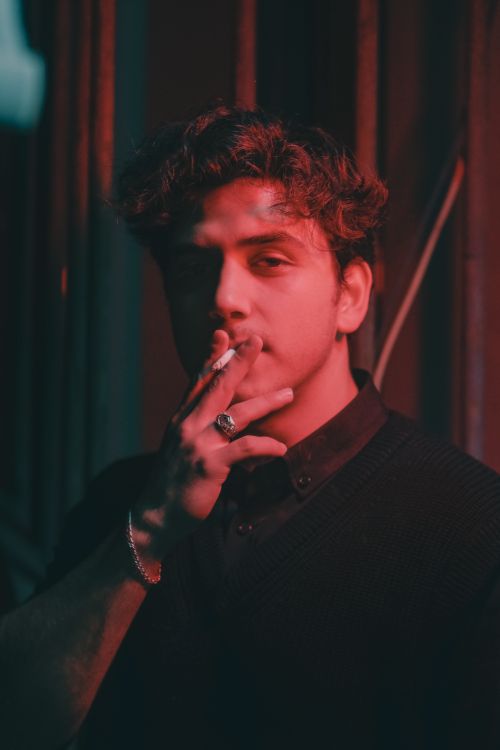 Free Portrait of a man smoking in a moody, red-lit setting, emphasizing lifestyle and atmosphere. Stock Photo