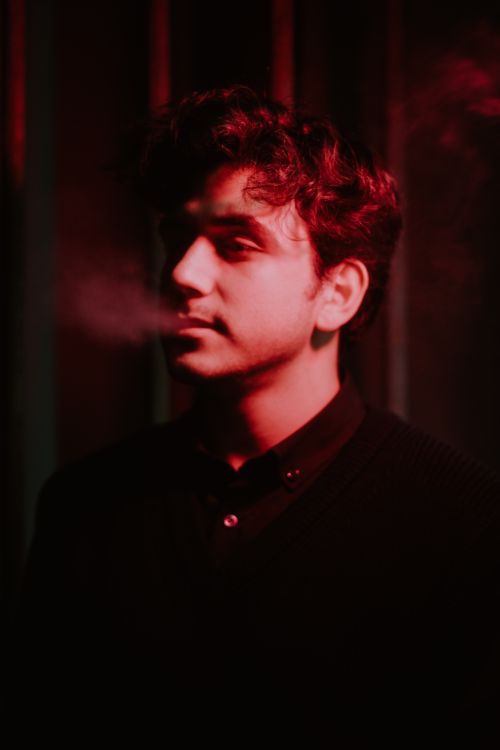 Free Moody portrait of a man in red lighting, exhaling smoke with a contemplative expression. Stock Photo