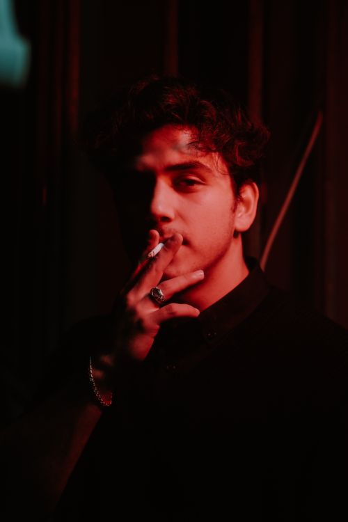 Free Portrait of a casually dressed man smoking a cigarette, illuminated by dramatic red lighting. Stock Photo