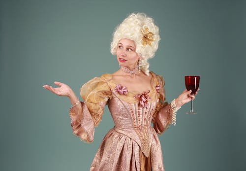 Free Woman in a Rococo-style dress holding a glass of red wine against a gray background. Stock Photo
