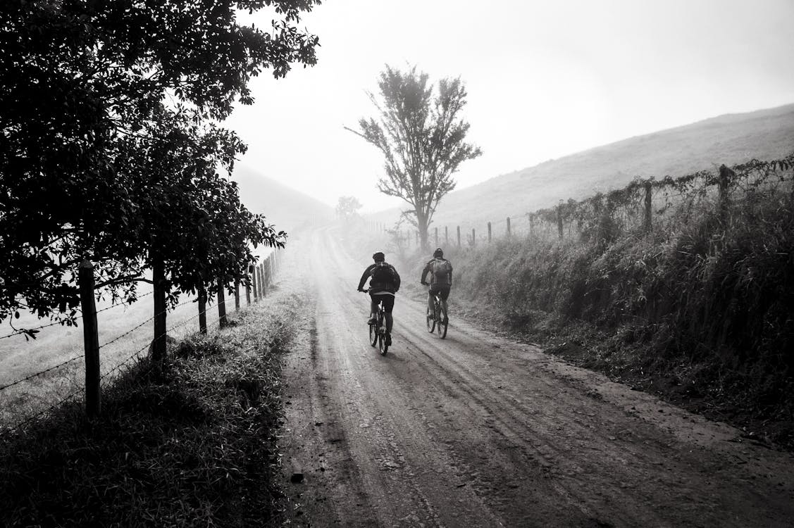 бесплатная Фотография в оттенках серого, на которой двое людей едут на велосипеде Стоковое фото