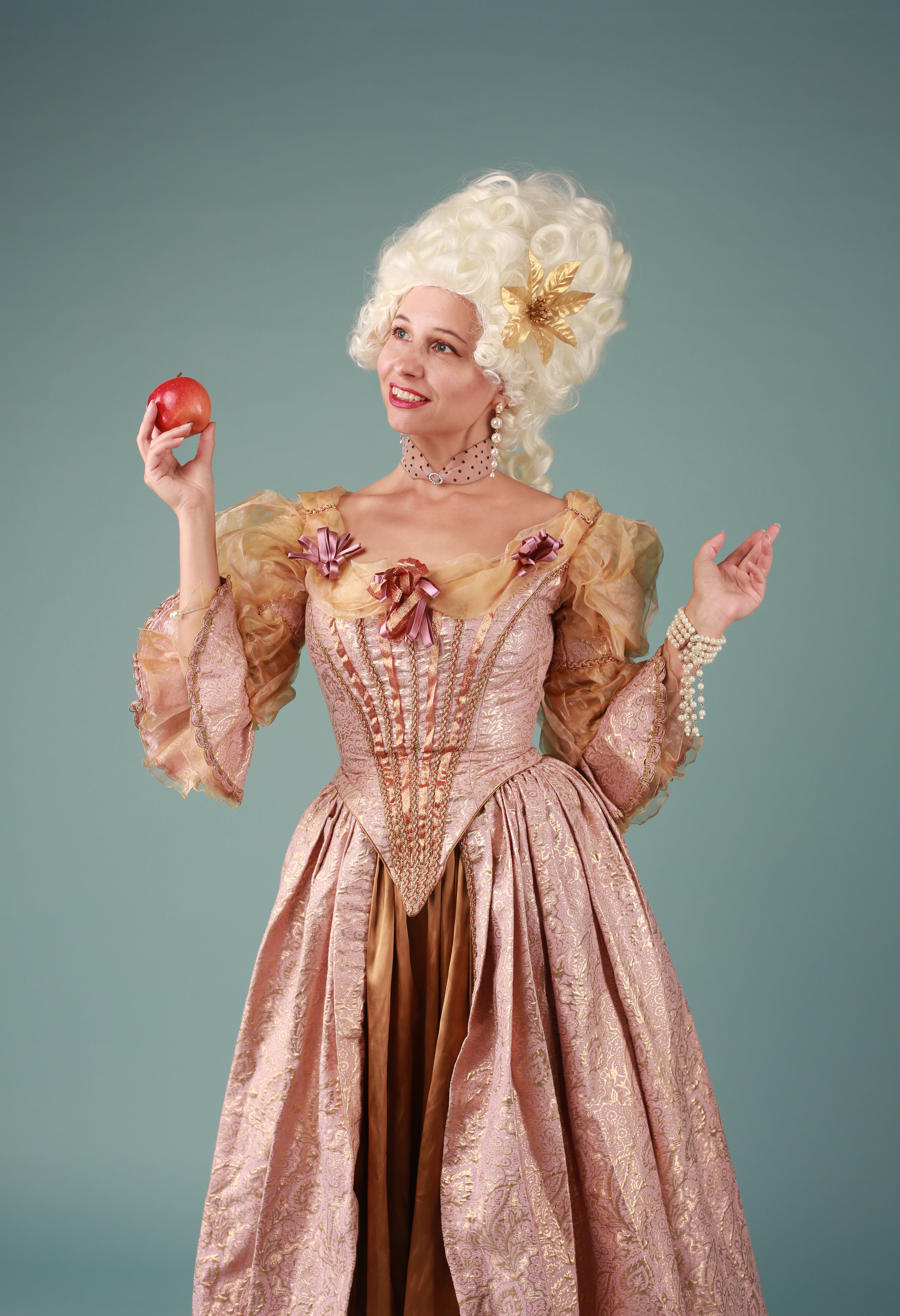 Woman in 18th-century dress posing with apple, showcasing elegant fashion.