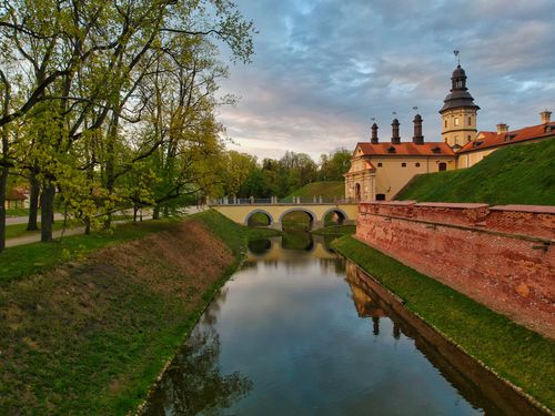 Free Beautiful view of Niasviž Castle in Belarus overlooking a tranquil canal surrounded by greenery and a bridge. Stock Photo