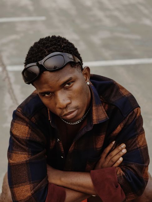 Stylish African American man with sunglasses on head and arms crossed, posing outdoors in plaid shirt.