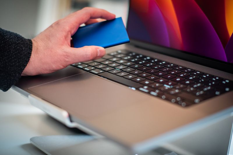 Close-up of a hand holding an external hard drive over a laptop keyboard, representing data backup