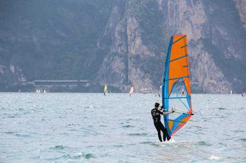 Free Man in Black Wetsuit Standing on Orange and Blue Sailboat during Daytime Stock Photo