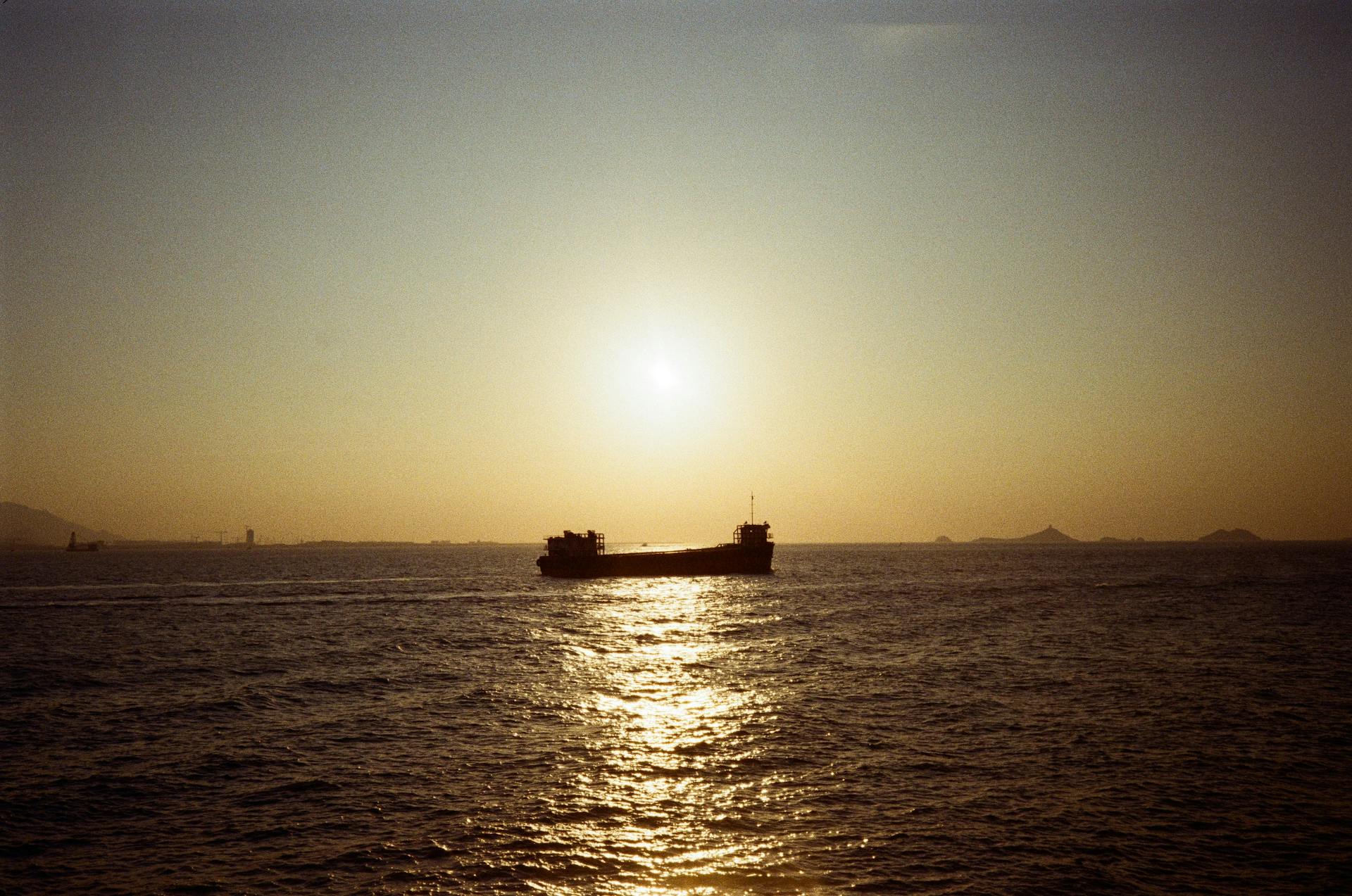 Silhouette of a cargo ship sailing in the ocean under a warm sunset horizon.