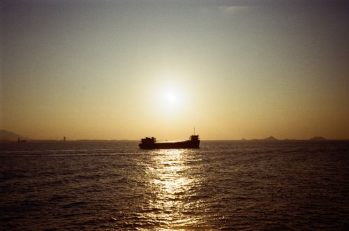Free Silhouette of a cargo ship sailing in the ocean under a warm sunset horizon. Stock Photo