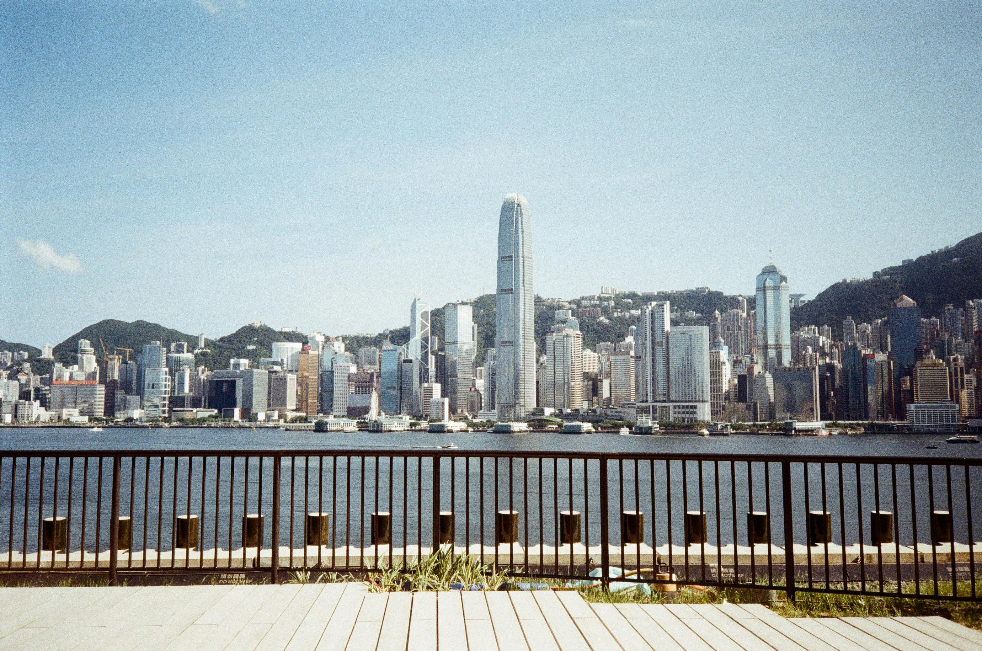 Panoramic view of Hong Kong's skyline from the waterfront, showcasing skyscrapers and a clear blue sky.