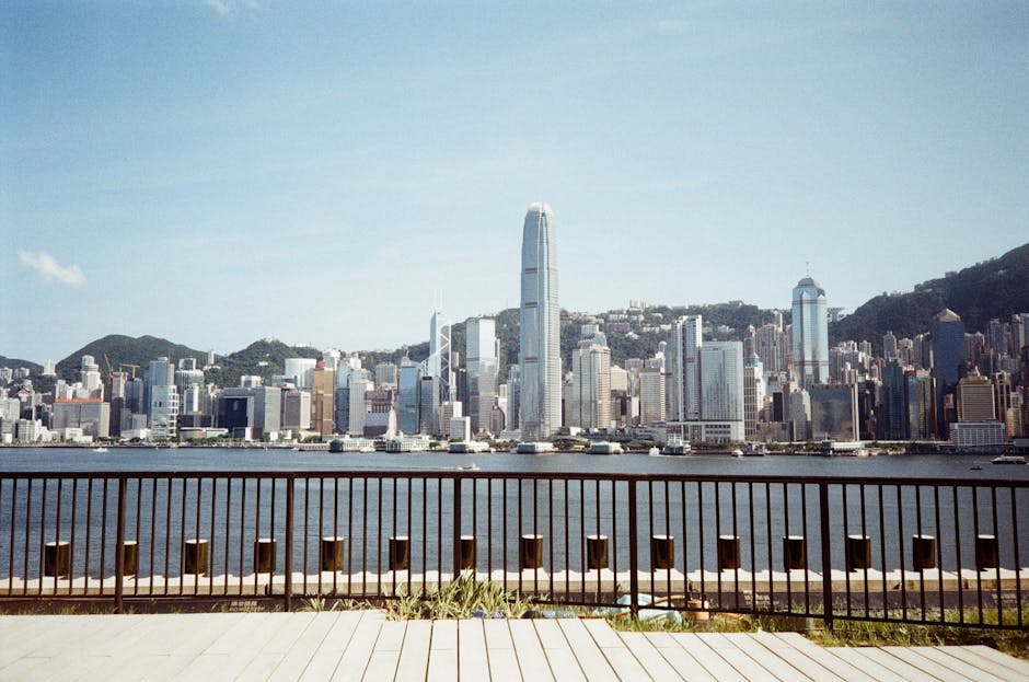 Panoramic view of Hong Kong's skyline from the waterfront, showcasing skyscrapers and a clear blue sky.