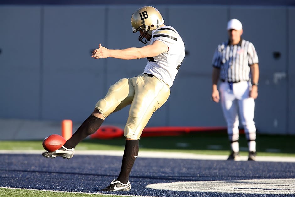 Football player kicking the ball during a game with referee in background.