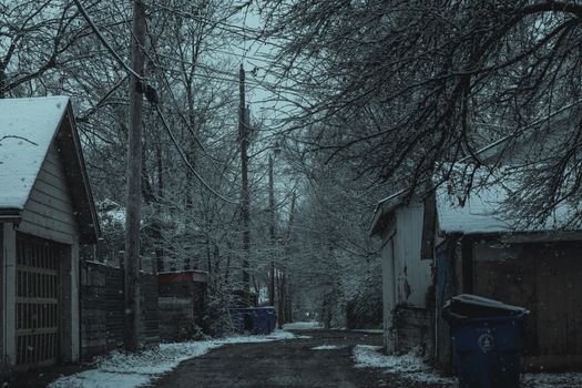 A peaceful, snow-covered village road on a cold winter evening, surrounded by quiet houses and trees.