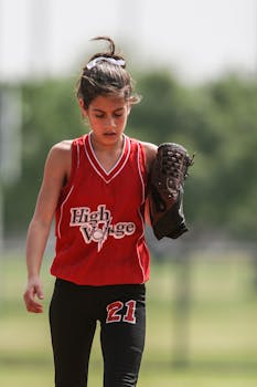 A young girl in a red uniform playing softball on a sunny day.