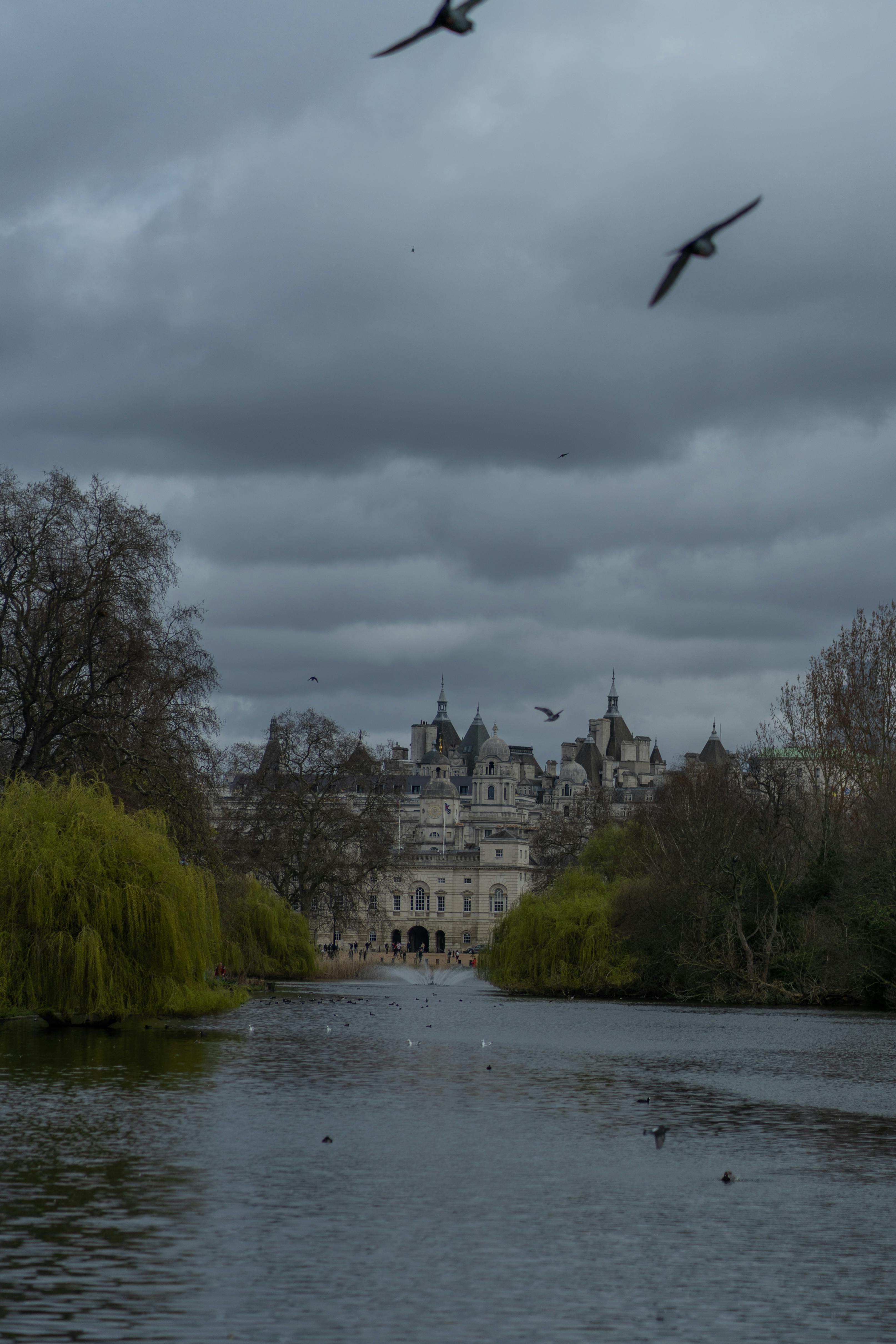 A tranquil view of St James's Park with a historic building in the background under cloudy skies.