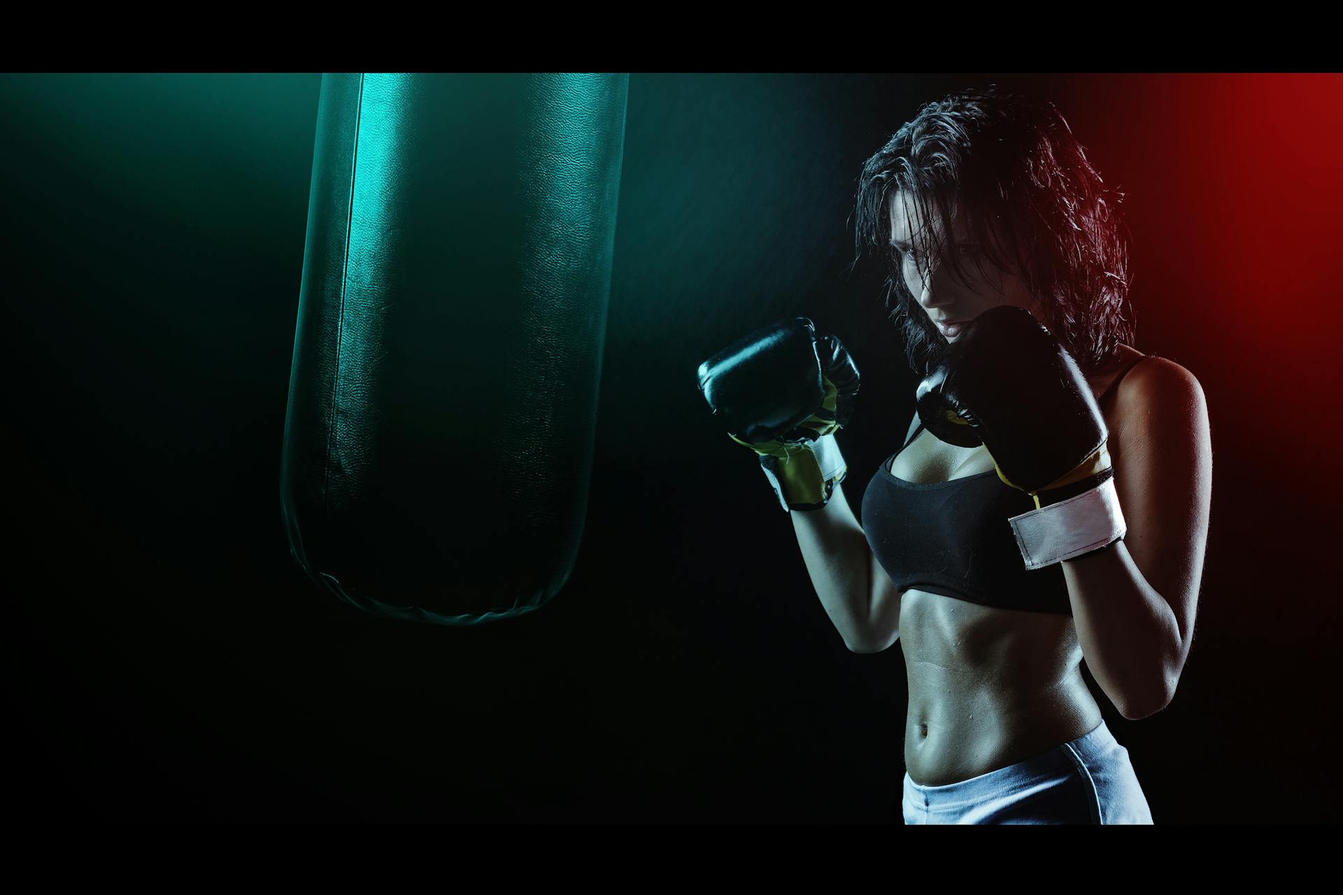 Woman in Boxing Gloves With Sports Bra Posing Boxing Style in Front of Punching Bag