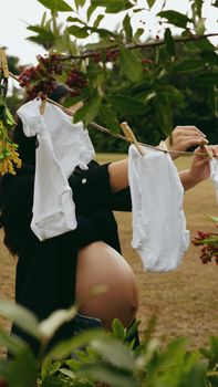 Pregnant woman outdoors hanging baby clothes with greenery in background, symbolizing motherhood. - Fotografer Sidoarjo