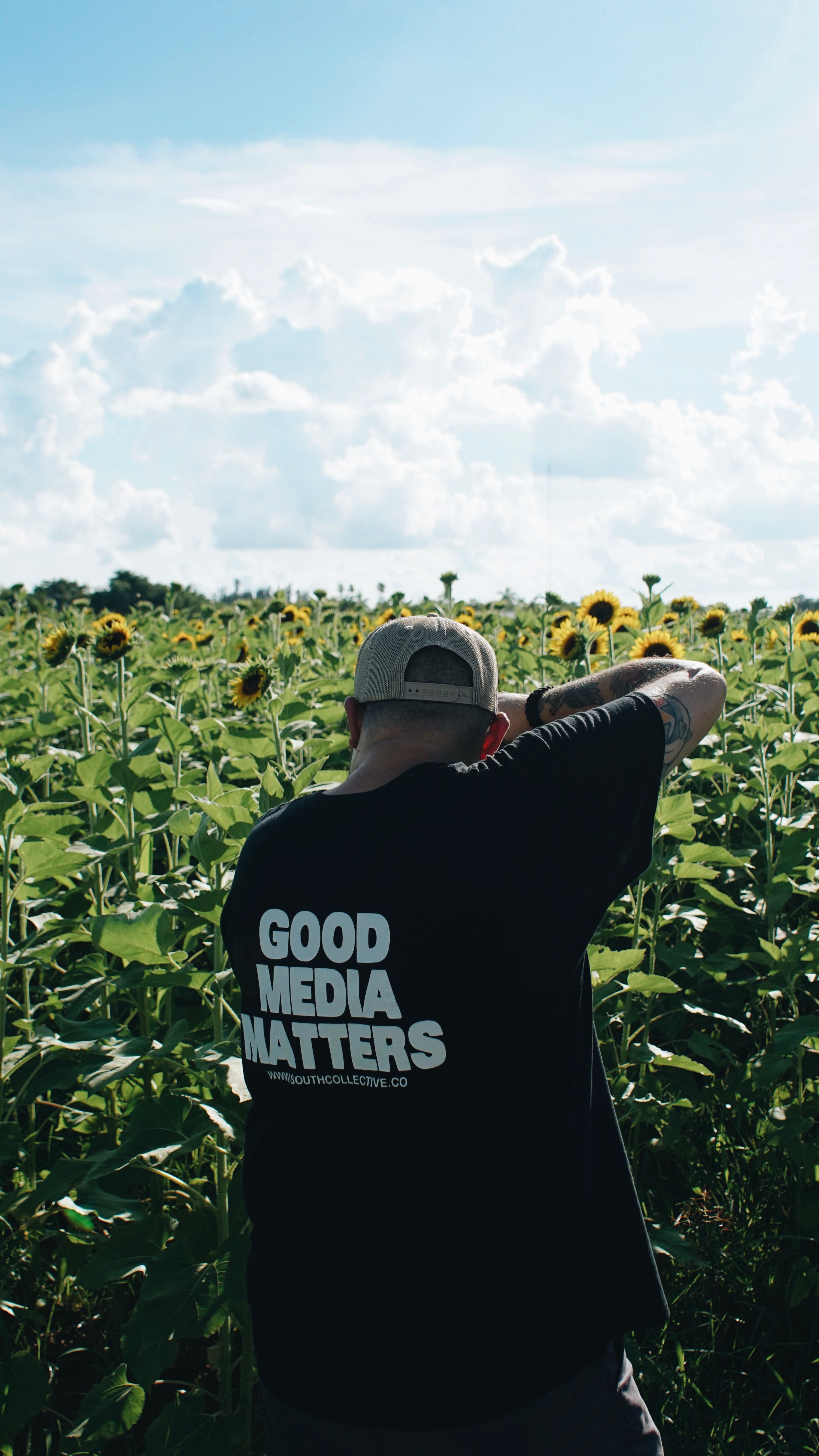 A man photographing sunflowers in a Miami field under a bright summer sky.