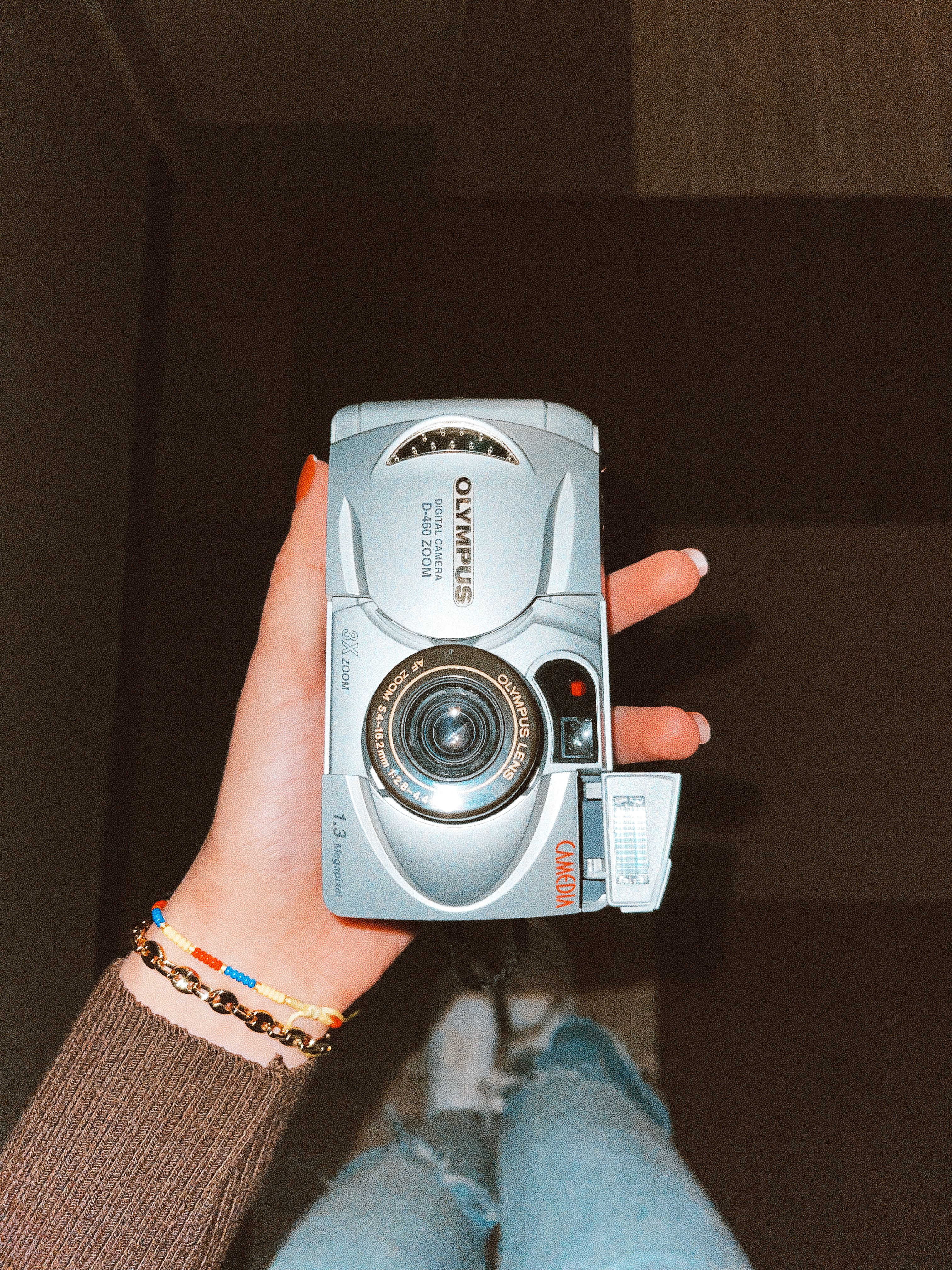 A person holds a vintage Olympus camera from a top view angle, showcasing the retro design.