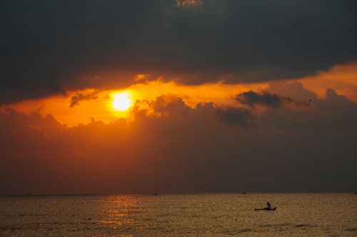 Free Vibrant sunset with dark clouds reflecting on a tranquil sea horizon. Stock Photo