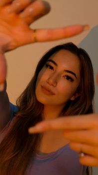 A young woman posing confidently with her hands framing her face, captured in a warm artistic light in Miami.