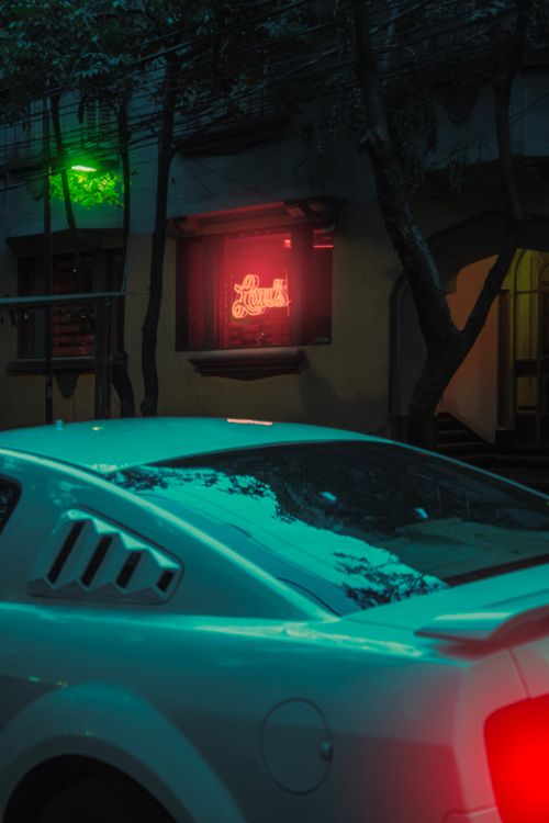 Free A sleek sports car parked under vibrant neon lights in an urban setting at night. Stock Photo