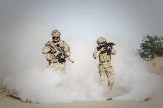 Two soldiers in full gear advancing through smoke during a military operation.