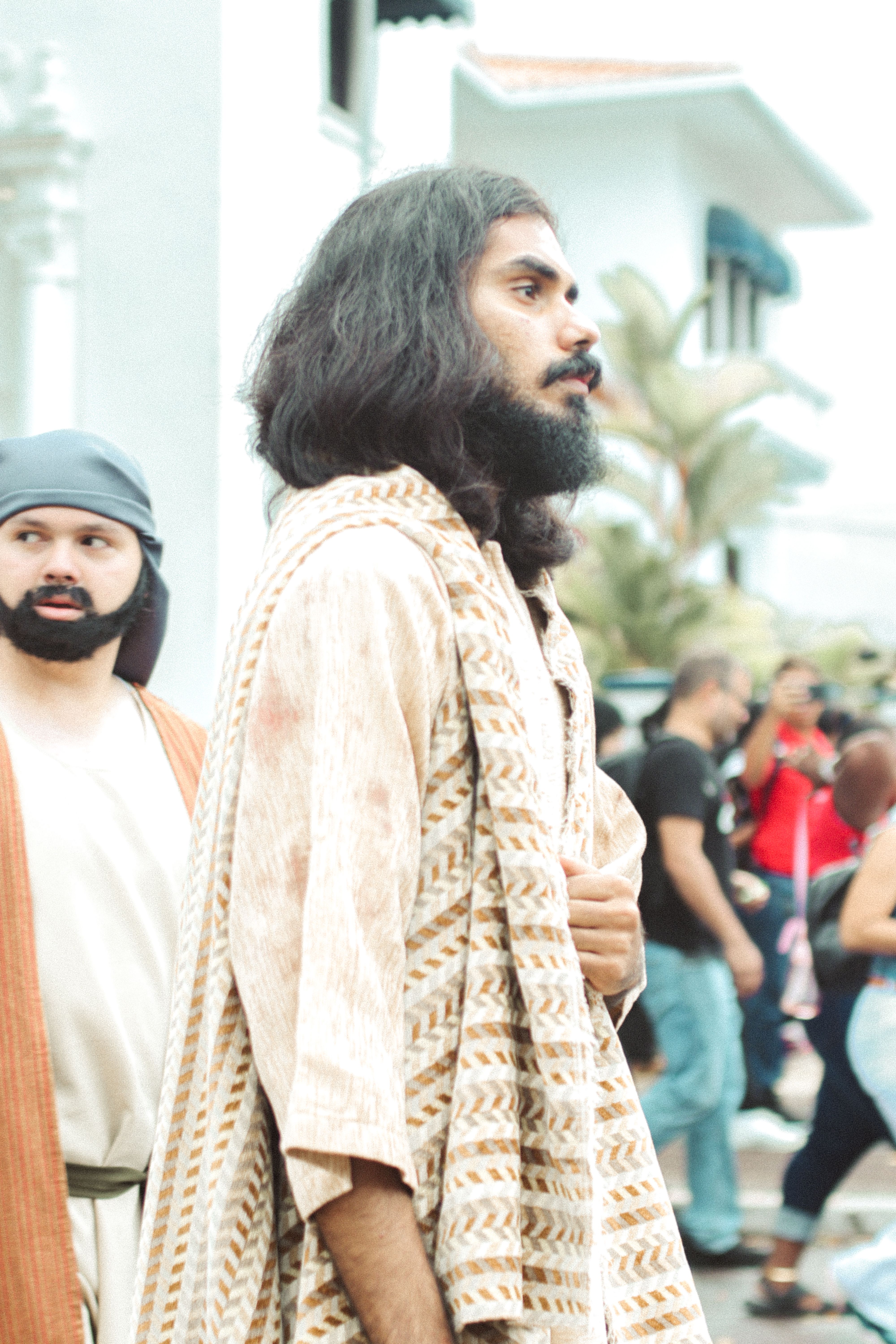 Men in traditional clothing walk through a crowded urban area, showcasing cultural fashion.