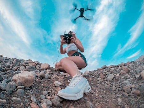 Woman operating a drone in a rocky desert landscape, capturing aerial footage with clear blue skies.