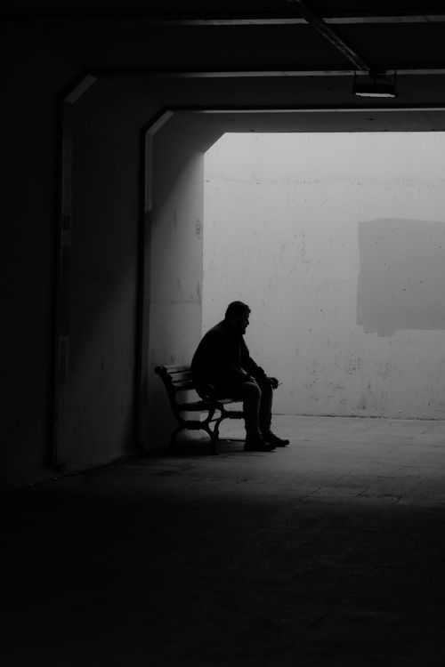 Free Dark silhouette of a person sitting alone on a bench in a tunnel with a moody atmosphere. Stock Photo