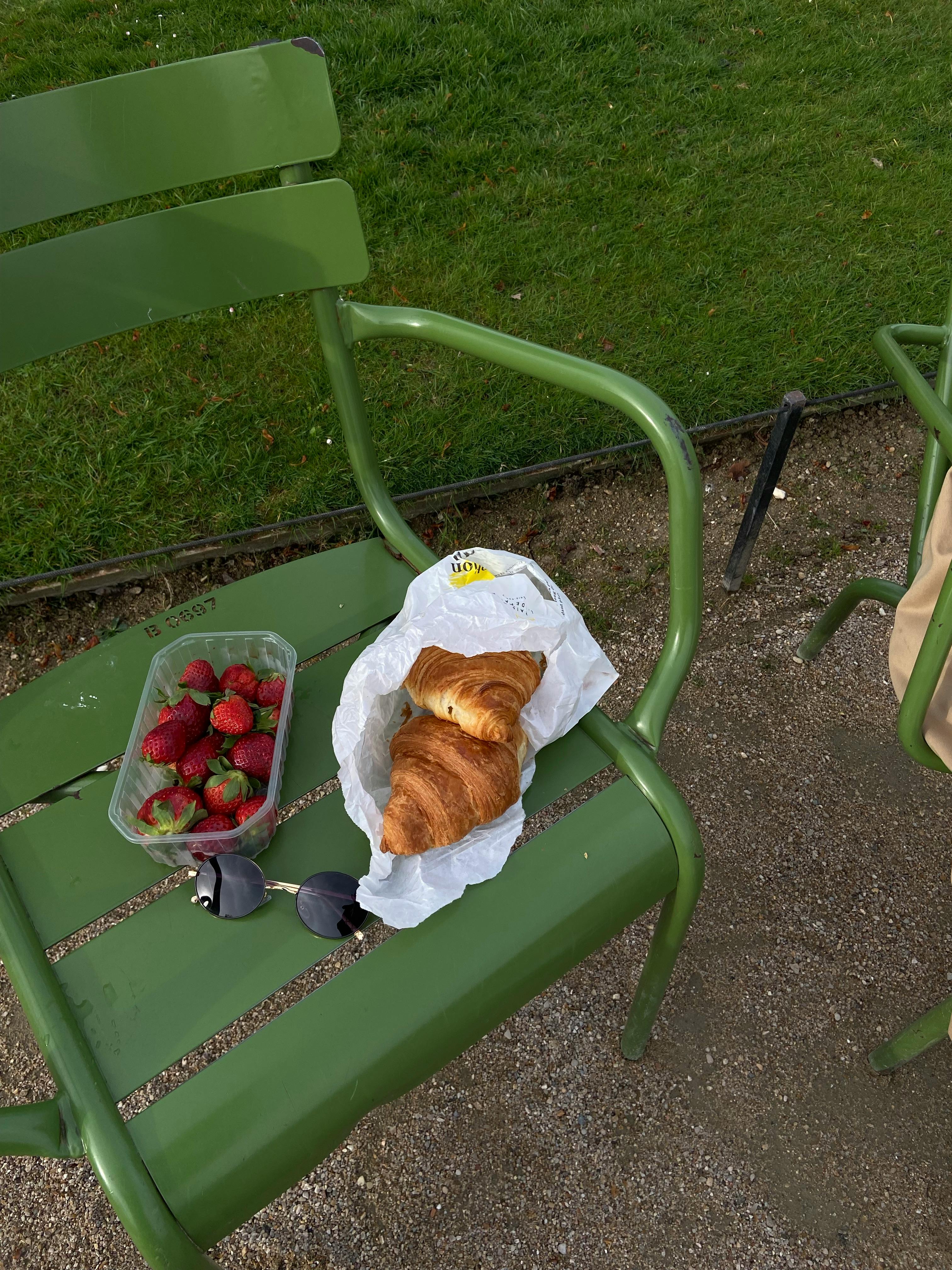 A serene park bench picnic with fresh croissant and strawberries, perfect for a Parisian afternoon.