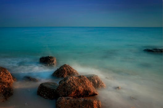 Peaceful seascape featuring rocks on a tranquil ocean shore under a clear sky.