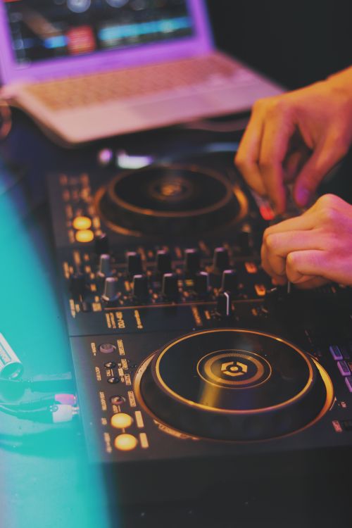 Free Close-up of DJ hands mixing music on a sound mixer at a lively nightclub. Stock Photo