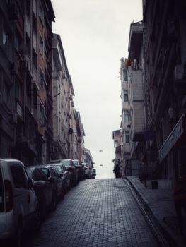 A quiet street lined with parked cars in a steep urban city setting.