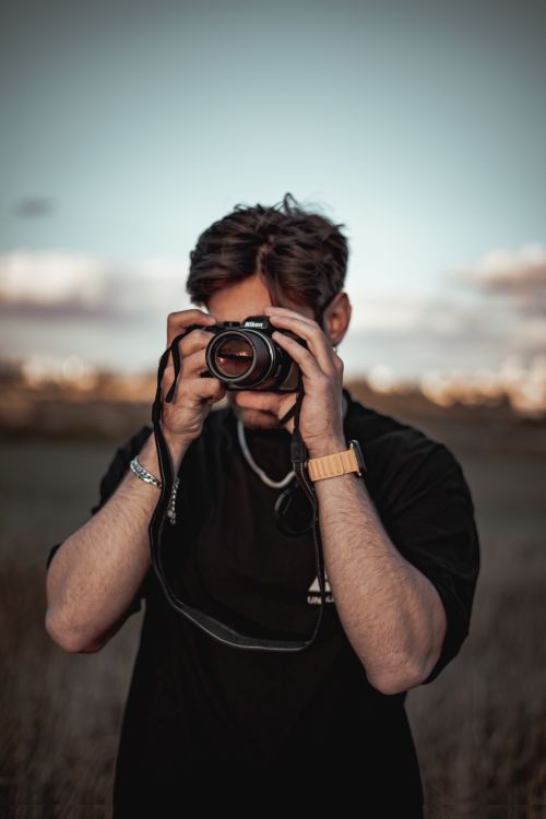 Free A young man in a black t-shirt takes photos outdoors during the day. Stock Photo
