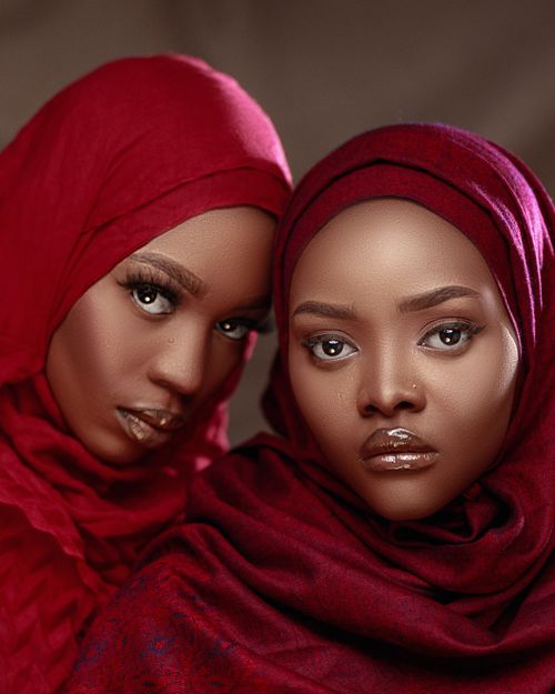Free Close-up portrait of two women wearing red hijabs, set against a brown background. Stock Photo