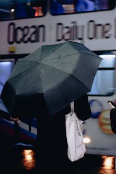 A person holds an umbrella on a rainy city street as bustling traffic passes by.