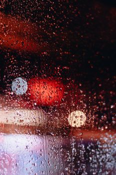 Blurry view of raindrops on a window with colorful bokeh night lights.