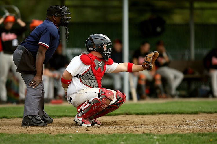 White And Red Baseball Player With Black Face Helmet And Brown Leather Mitts