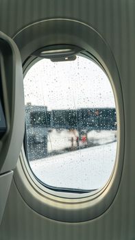 A rainy airport day viewed through an airplane window, capturing raindrops and blurred tarmac.